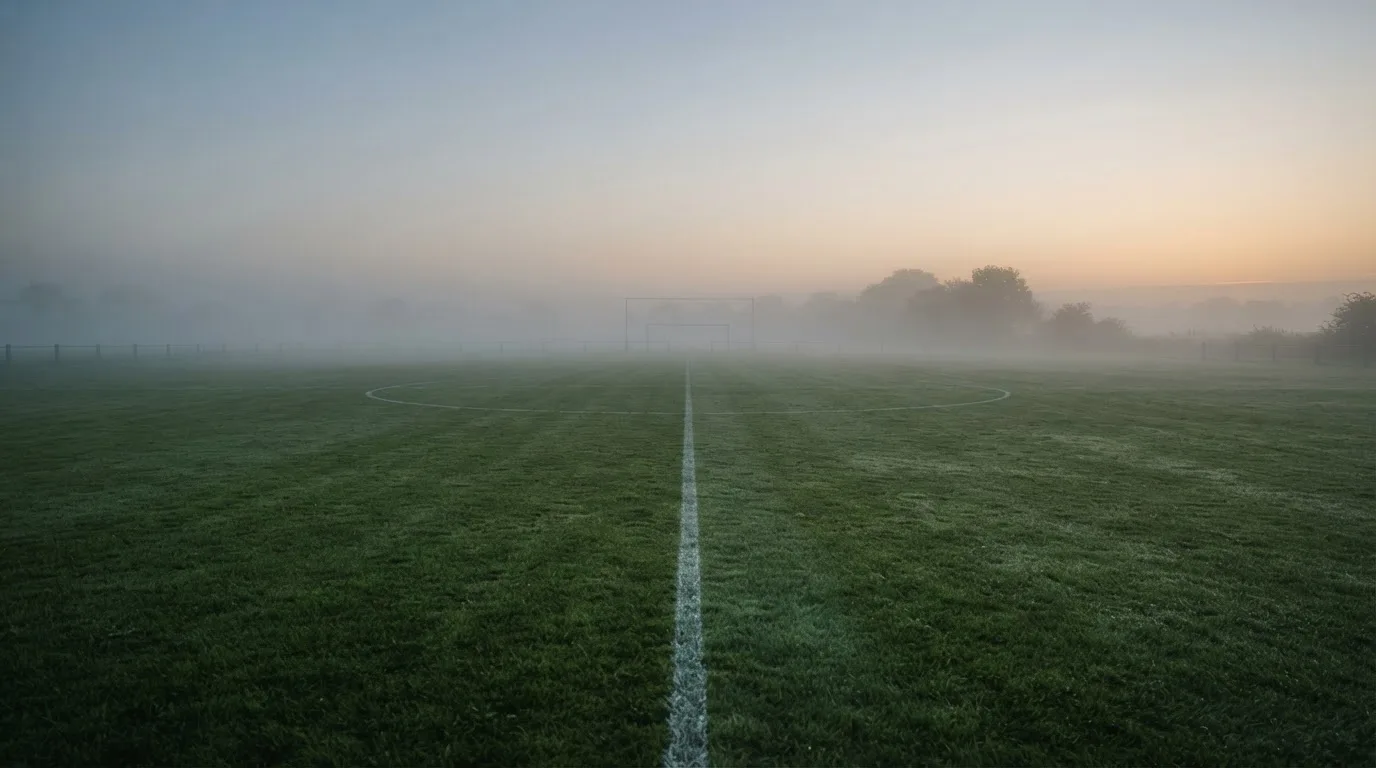 Ein leeres Fußballfeld im Morgennebel, die Mittellinie verliert sich im Dunst, kein Mensch ist zu sehen.