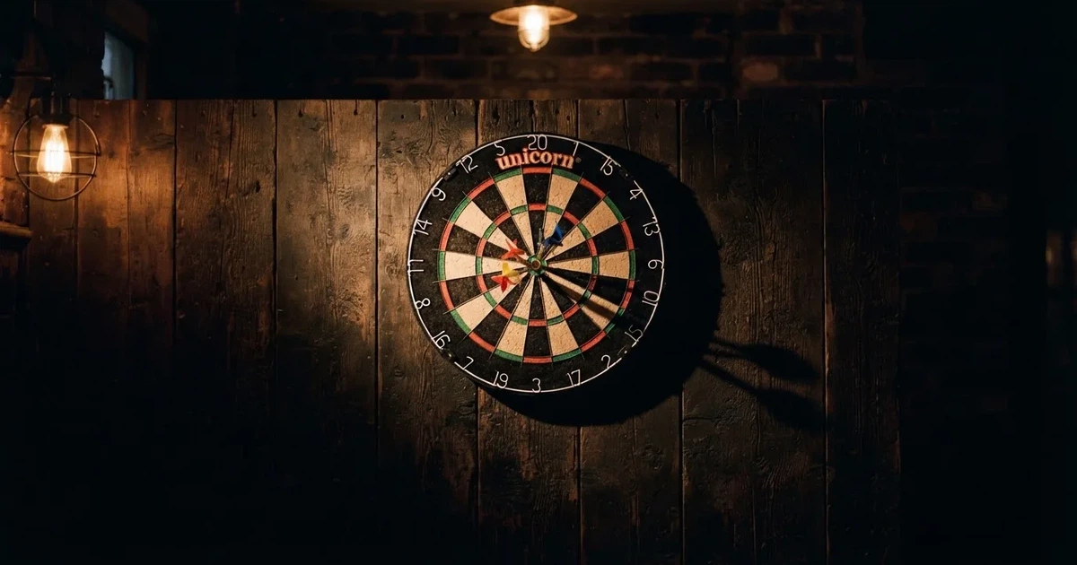 Eine Dartscheibe an einer Holzwand in einem schwach beleuchteten Raum, drei Pfeile stecken nahe der Mitte, warmes Licht von der Seite.